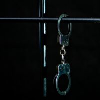 PoliceHandcuffsAreFastenedToTheBarsOfTheCell